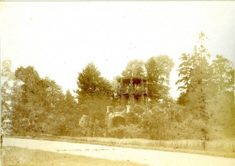 Park przy pałacu w Będlewie ze ścieżką widziany w dzień. W tle zabudowanie otoczone drzewami.