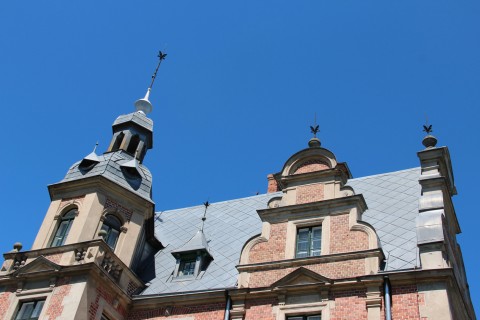 Fragment metalowego dachu pałacu w Kobylnikach widziany z dołu w dzień. W trzech z czterech wieżyczek okna.